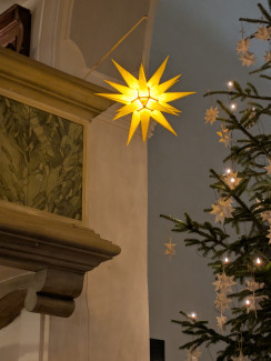 Ein Herrnhuther Stern mit einem mit Strohsternen verziertem Christbaum.